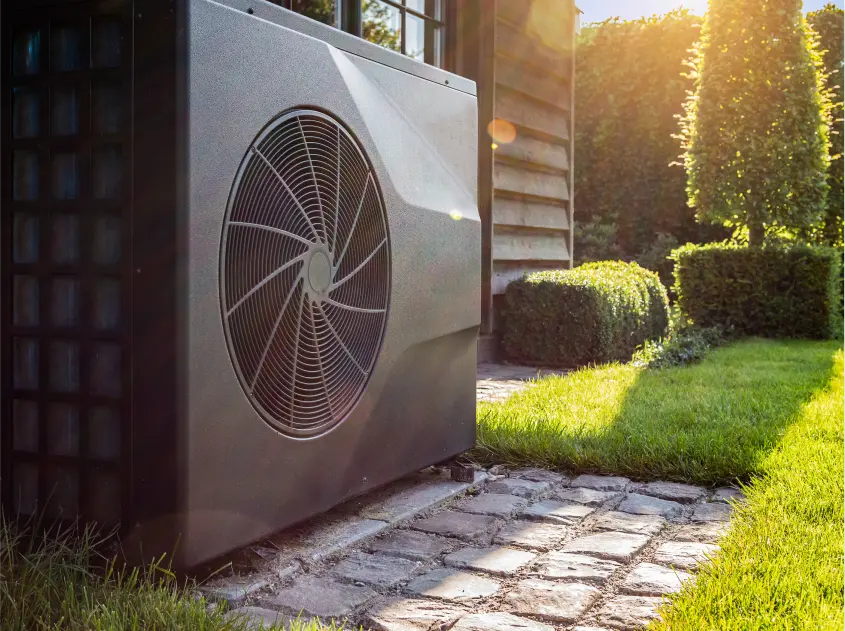 Residential heat pump outdoor unit installed near a home, shown in sunlight with landscaping—photo for heat pump installation and repair services in Spokane, WA.
